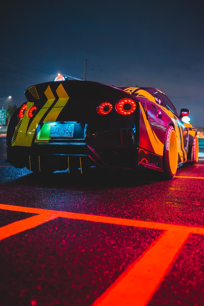 Sport car with spoiler on trunk and round red tail lights on wet asphalt road at night